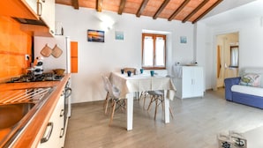 Una cucina compatta con piano cottura a gas, mobili bianchi e un'area pranzo con tavolo e sedie.