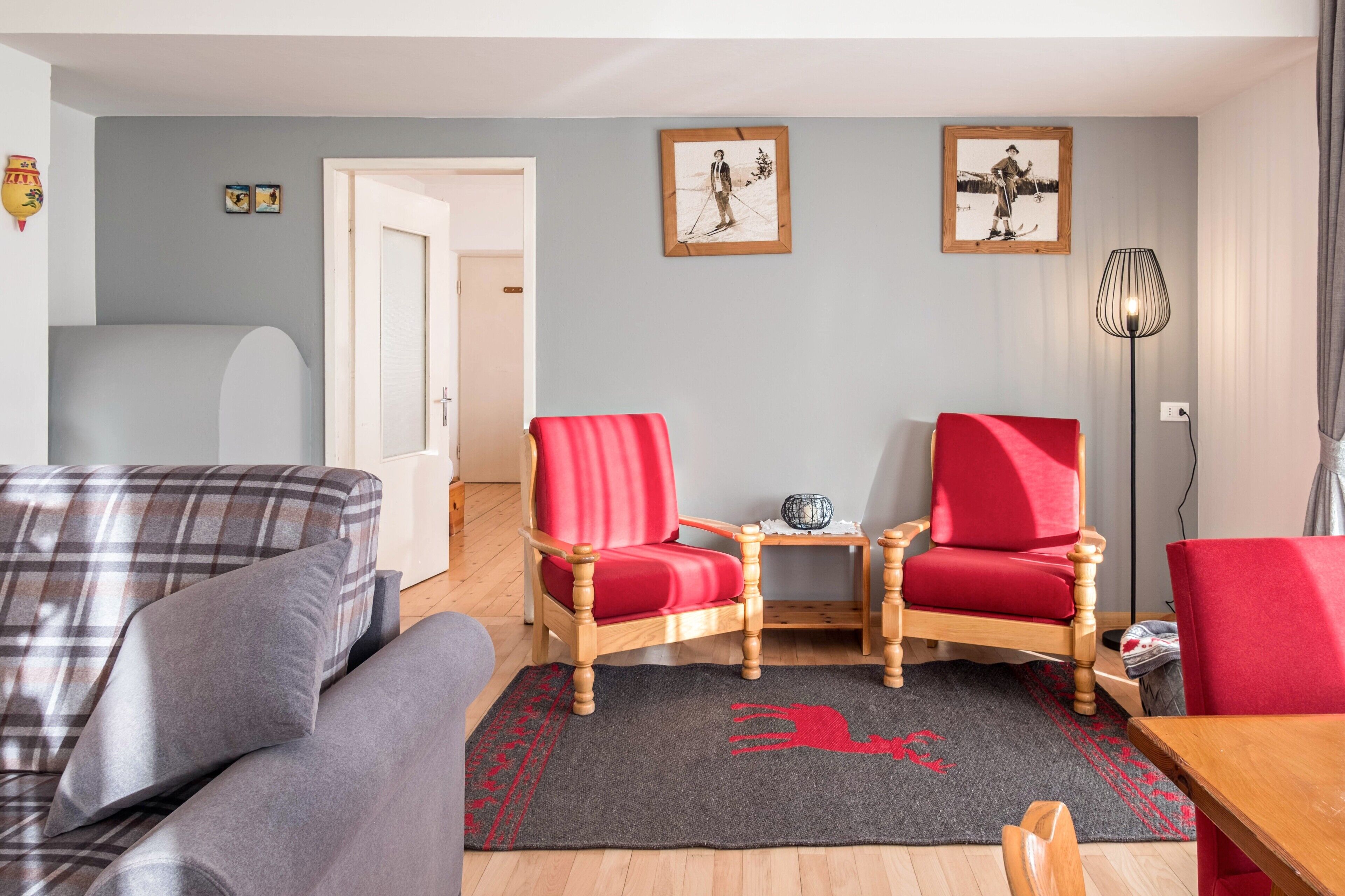 Een woonkamer met een geruit bankstel, twee rode stoelen, een houten salontafel en een vloerkleed met een rood ontwerp.