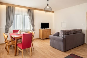 Un salon comprenant un canapé, une table à manger avec des chaises, un téléviseur et un meuble en bois.