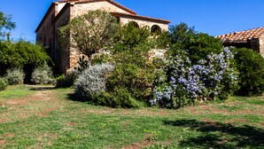 Un bâtiment en pierre doté de fenêtres en arc de cercle, entouré d’une végétation luxuriante et de plantes en fleurs.