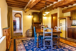 Un comedor con una mesa de madera, sillas y un tapete. Hay una cocina con un refrigerador y armarios.