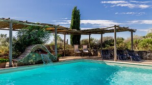 Une piscine agrémentée d’un élément décoratif aquatique, de chaises longues et d’une pergola.