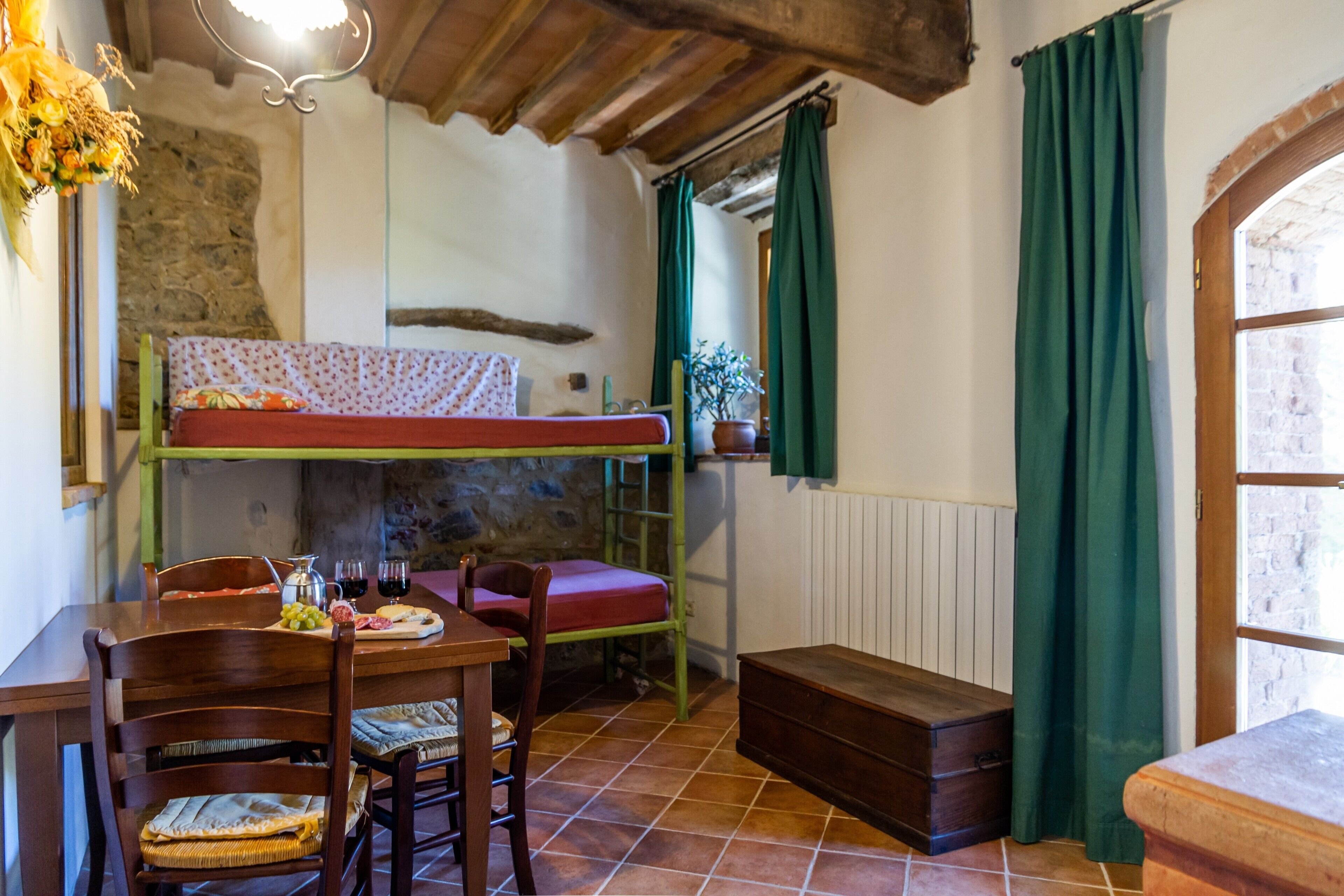 A rustic room with a bunk bed, wooden furniture, a dining table with chairs, and a window with curtains.