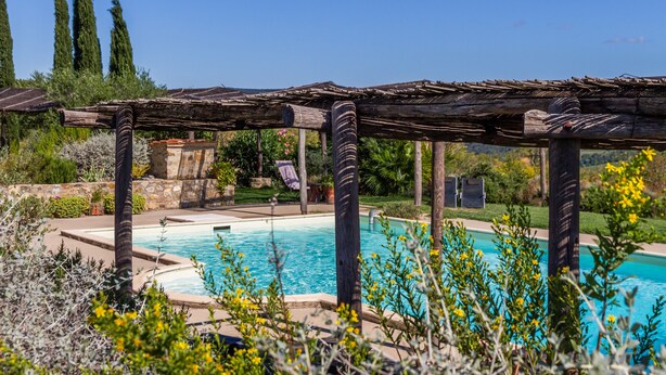Een zwembadgedeelte met een pergola, stenen muren en uitzicht op het omliggende landschap.