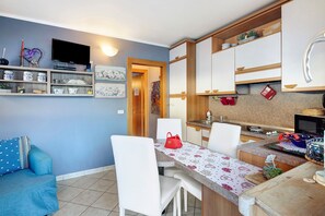 Un espace de vie compact comprenant un coin repas, une kitchenette et un téléviseur fixé au mur.