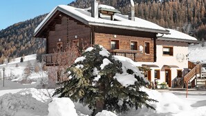 Un chalet en bois, avec un toit enneigé, un balcon et une vue sur les montagnes.