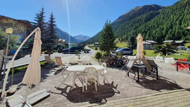Une terrasse extérieure avec des tables et des chaises, une vue sur les montagnes et un ciel dégagé.