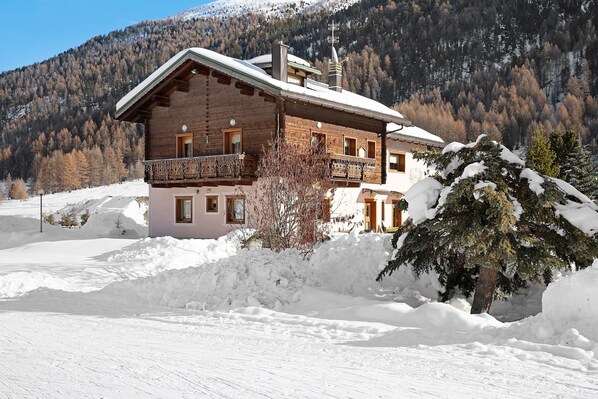 Un chalet en bois doté d’un balcon, entouré de neige et adossé à une montagne boisée.