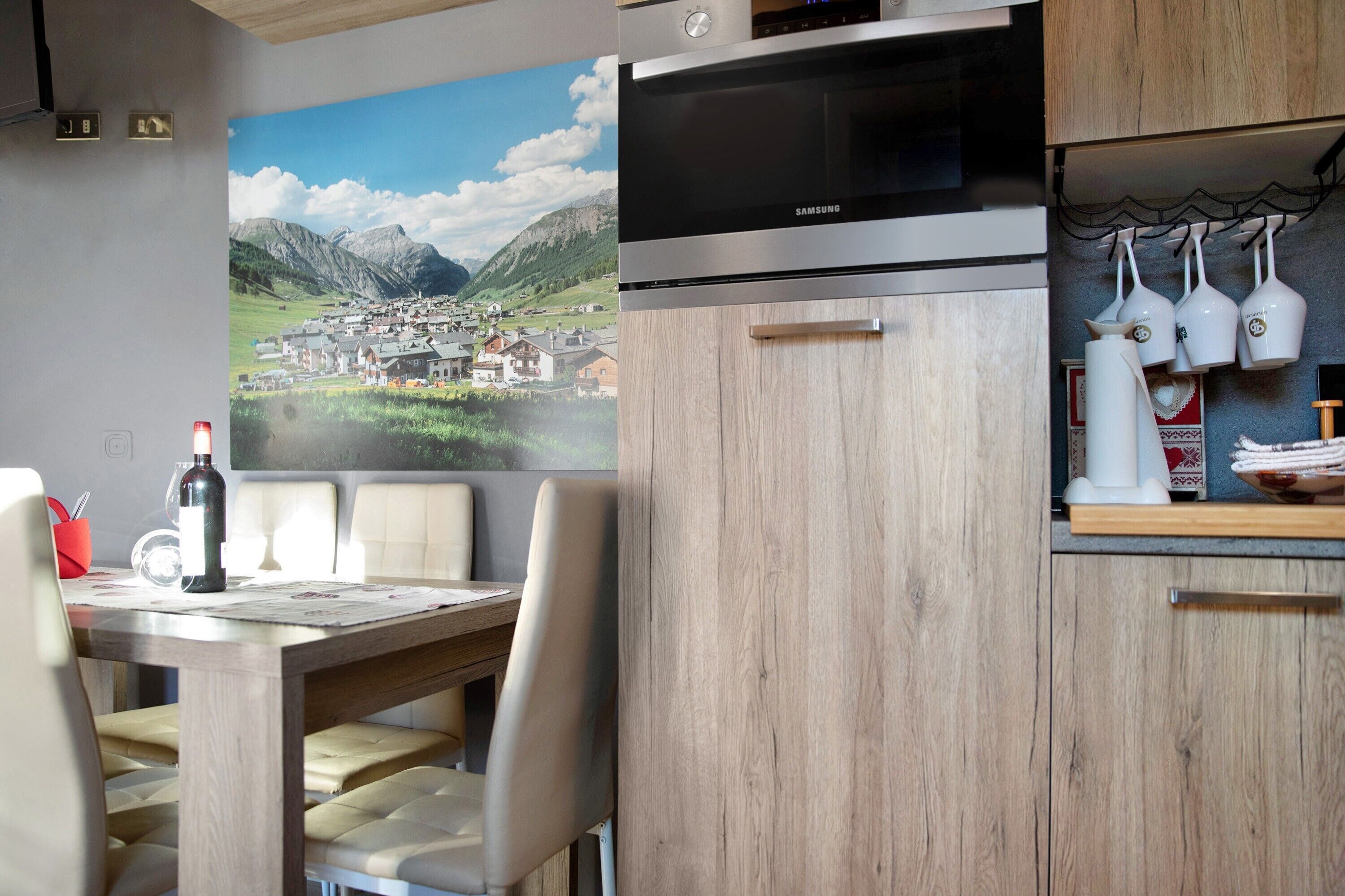 A modern kitchen with a Samsung oven, a dining table with chairs, and a scenic mural on the wall.