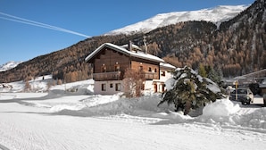 Eine Holzhütte mit Balkon, umgeben von schneebedeckten Bergen und einem klaren Himmel.