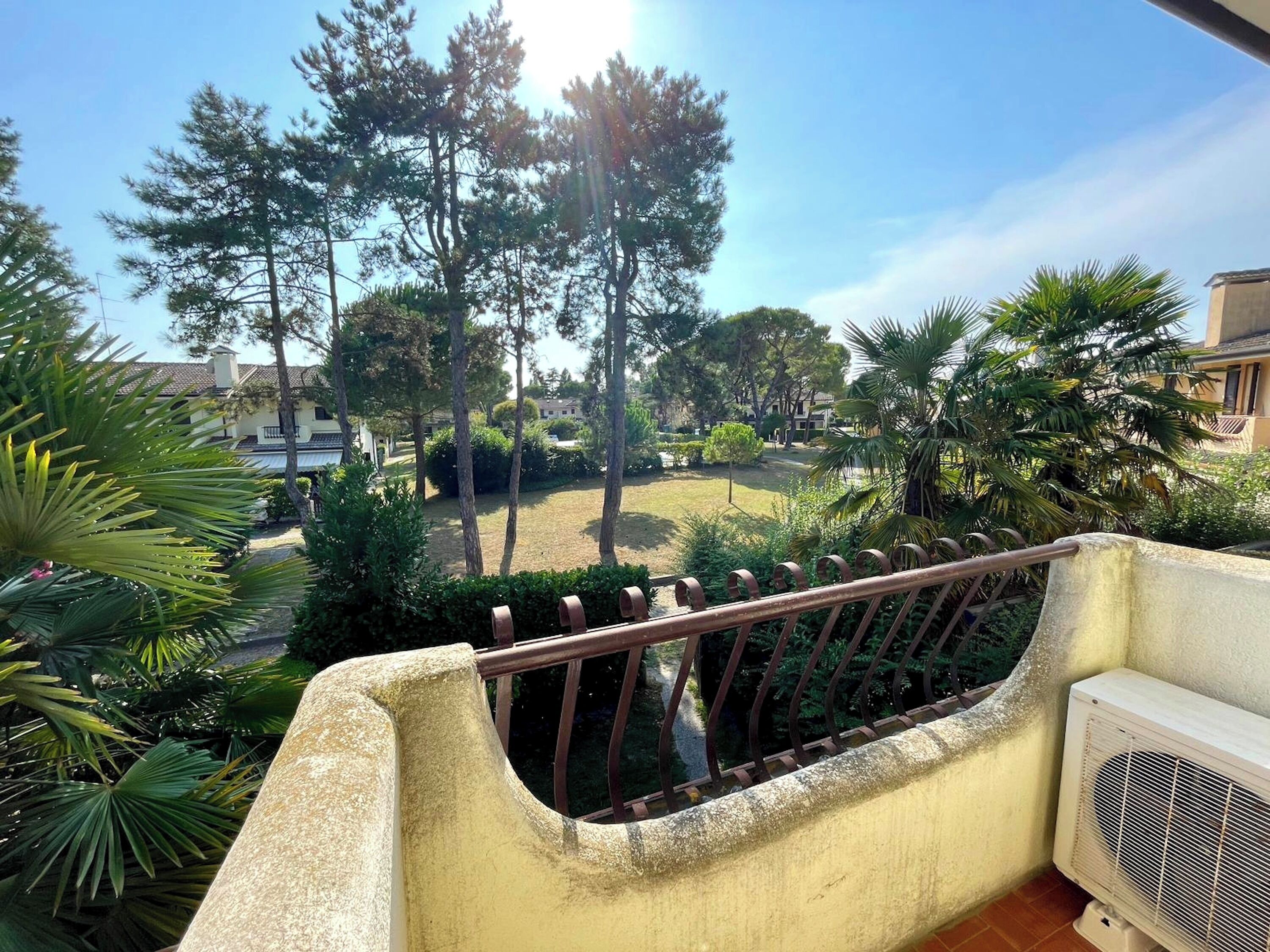 A balcony with a view of a landscaped garden, including trees and a lawn.