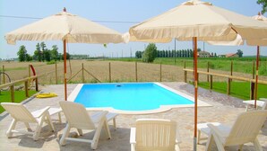 Ein Swimmingpool mit weißen Liegestühlen und beigen Sonnenschirmen, umgeben von einer Steinterrasse.