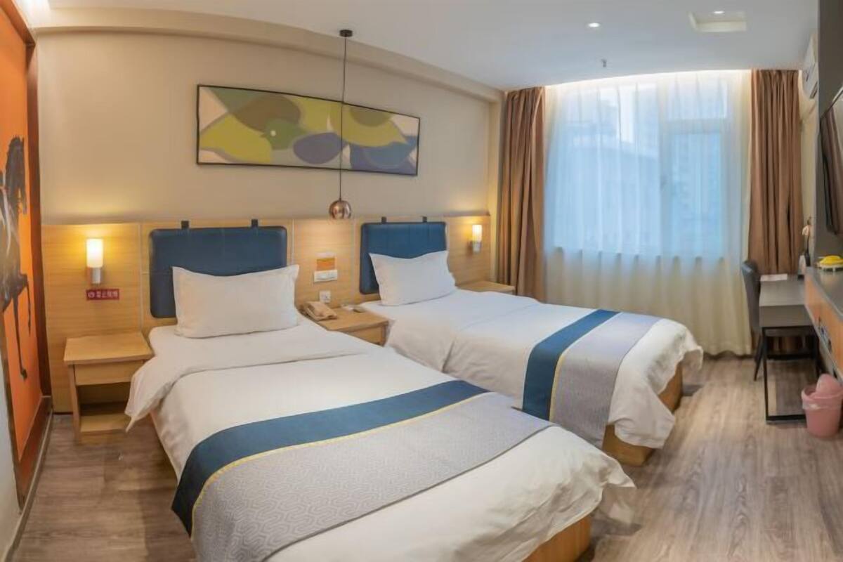 A hotel room with two beds, a desk, and a large window with curtains.
