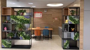 A modern dining area with a wooden table and chairs, surrounded by black shelving units with plants. - Jiatai Chain Hotel Dandonghuanghai Market Store (Donggang)