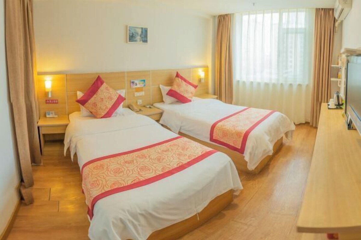 Habitación de hotel con dos camas, piso de madera, televisor y escritorio.