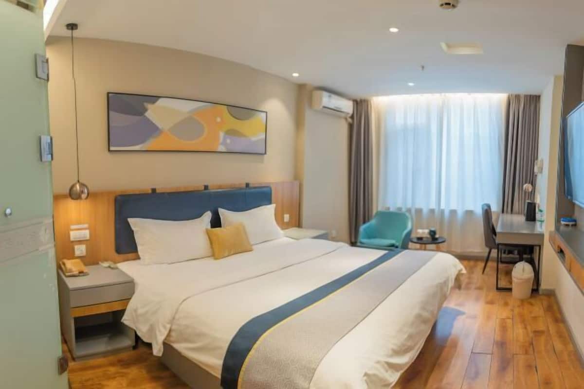 A hotel room with a large bed, a desk, a chair, and a television.