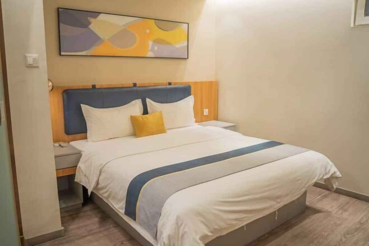A neatly made bed with a blue headboard, white bedding, and a single yellow pillow.