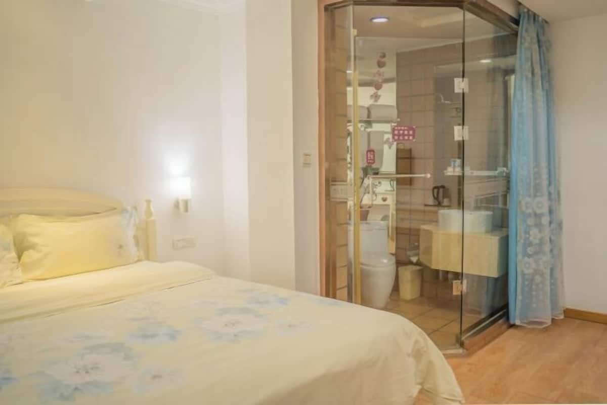 A bedroom with a bed, a glass shower enclosure, and a bathroom visible through the glass.