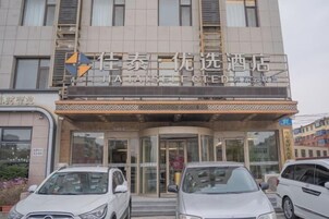 Entrada de hotel con diseño moderno, fachada de vidrio y acceso curvo. Hay coches estacionados frente al edificio, que tiene varios pisos con ventanas visibles.