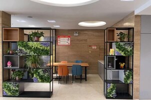 Un interior moderno con comedor, dos estanterías negras con plantas, pared de madera y un letrero rojo.
