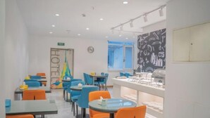 A modern dining area with tables and chairs, a kitchen counter, and a chalkboard wall. - Jiatai Chain Hotel Dandonghuanghai Market Store (Donggang)
