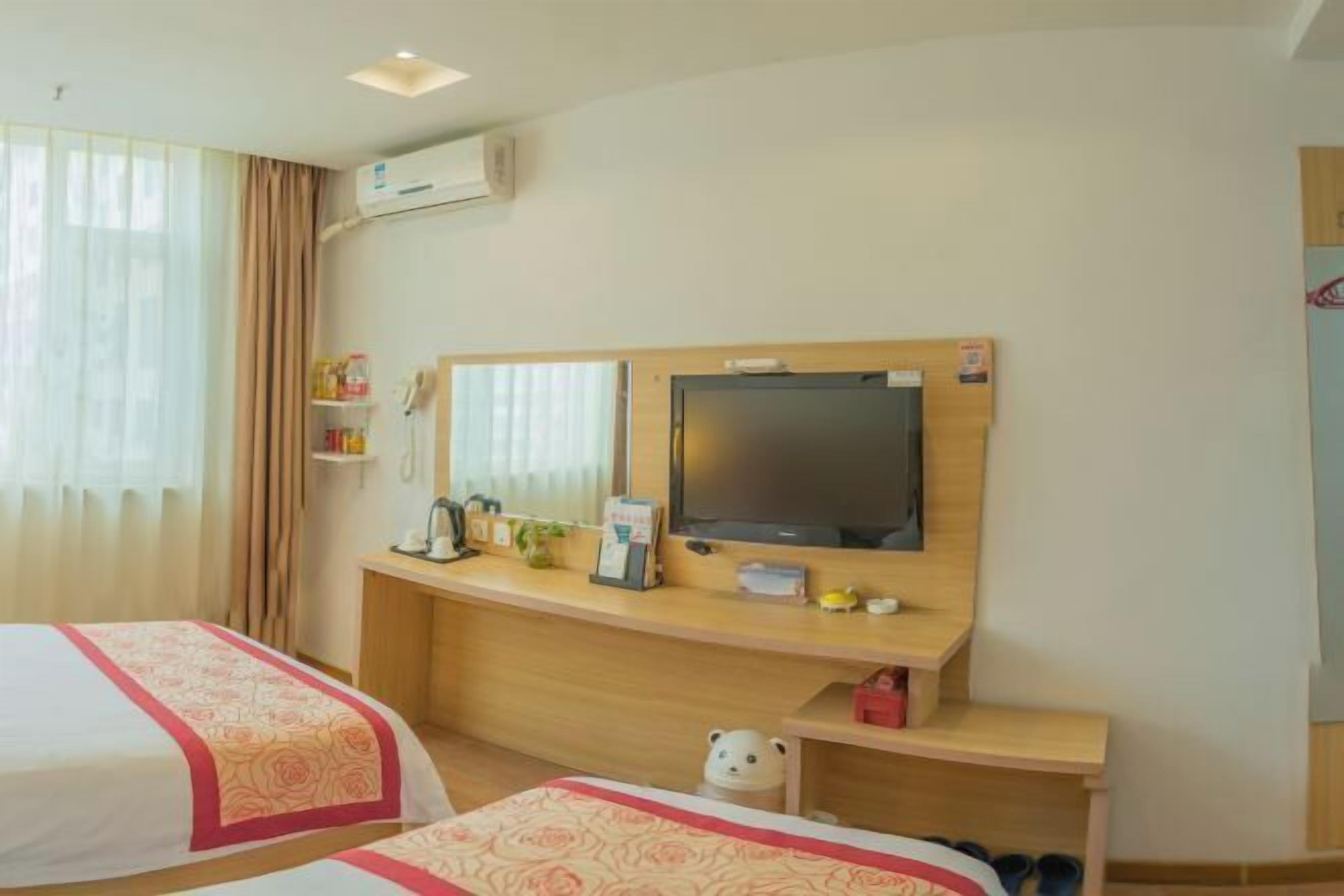 A hotel room with two beds, a desk with a television, a small table, and a teddy bear.