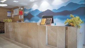 A reception desk with a mountain mural, a clock, and framed certificates. - Jiatai Chain Hotel Dandonghuanghai Market Store (Donggang)