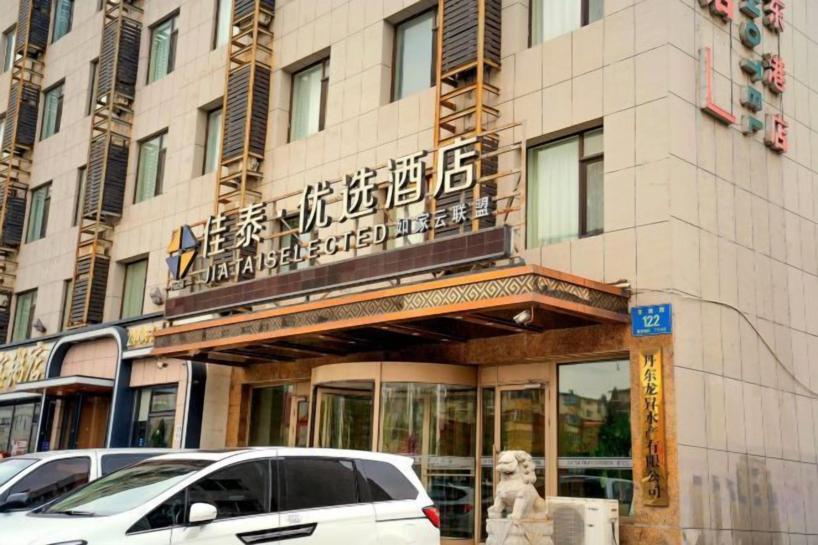 A hotel entrance with a sign indicating it is a 'JATAI SELECTED' establishment. There are cars parked in front, and a statue is visible to the right of the entrance.