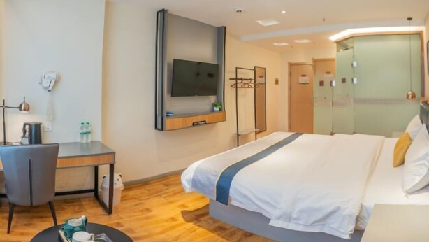 A modern hotel room with a large bed, a desk with a chair, a flat-screen TV mounted on the wall, and a small round table with a tray of cups and a teapot. - Jiatai Chain Hotel Dandonghuanghai Market Store (Donggang)