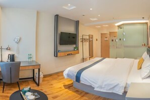 A modern hotel room with a large bed, a desk with a chair, a flat-screen TV mounted on the wall, and a small round table with a tray of cups and a teapot. - Jiatai Chain Hotel Dandonghuanghai Market Store (Donggang)