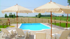 Une piscine entourée de chaises longues blanches et de parasols beiges.