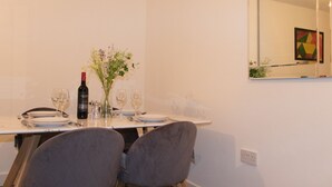 Una mesa de comedor con platos, cubiertos, copas de vino y una botella de vino. Hay dos sillas frente a la mesa.