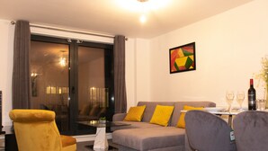 Una sala de estar moderna con un sofá gris, cojines amarillos, una mesa de comedor con sillas y un gran ventanal con cortinas.