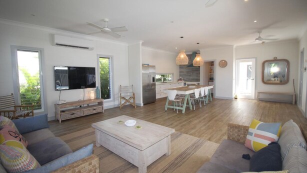 A spacious living room with a large TV, a dining area, and a kitchen with modern appliances. - Sandy Toes Beach House (HORSESHOE BAY)