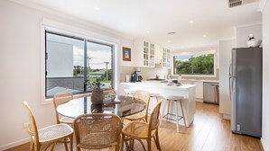 A modern kitchen with a central island, white cabinetry, and a large window offering a view of greenery. - Pet Friendly - Brooklyn Beach Abode Walk to the beach (Safety Beach)