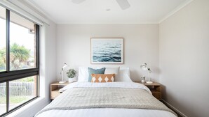 A bedroom with a large bed, two bedside tables, a window with a view of greenery, and a framed picture on the wall. - Pet Friendly - Brooklyn Beach Abode Walk to the beach (Safety Beach)