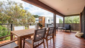 A wooden deck with a table and chairs, overlooking a garden and a modern building. - Pet Friendly - Brooklyn Beach Abode Walk to the beach (Safety Beach)