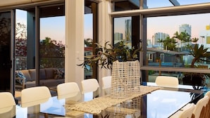 Ein moderner Essbereich mit einem Glastisch, weißen Stühlen und einem großen Fenster mit Blick auf die Stadt.