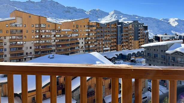Un complejo turístico en la montaña cubierto de nieve, con edificios de varios pisos, balcones y una vista despejada de las montañas.