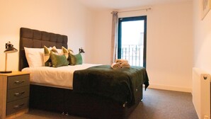 A neatly made bed with a dark headboard, a bedside lamp, and a window with curtains.