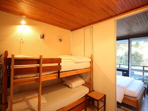 Quarto com beliche, teto de madeira e janela com vista para uma varanda.