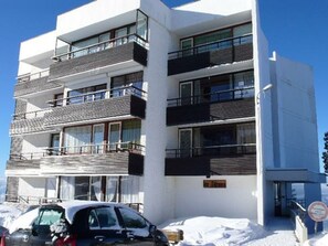 A multi-story building with balconies, a sign indicating a business or office, and a car parked in front.