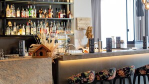 A bar area with shelves of liquor bottles, a wooden house decoration, and floral upholstered chairs. - DORMERO Hotel Freiburg (Freiburg im Breisgau)