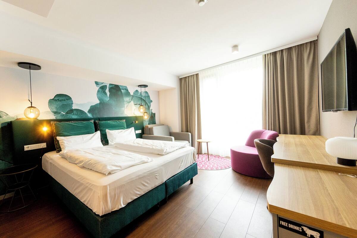 A hotel room with a bed, a desk, a chair, and a TV.