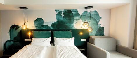 Habitación de hotel con cama, dos mesitas de noche, una silla y un cuadro abstracto en la pared.
