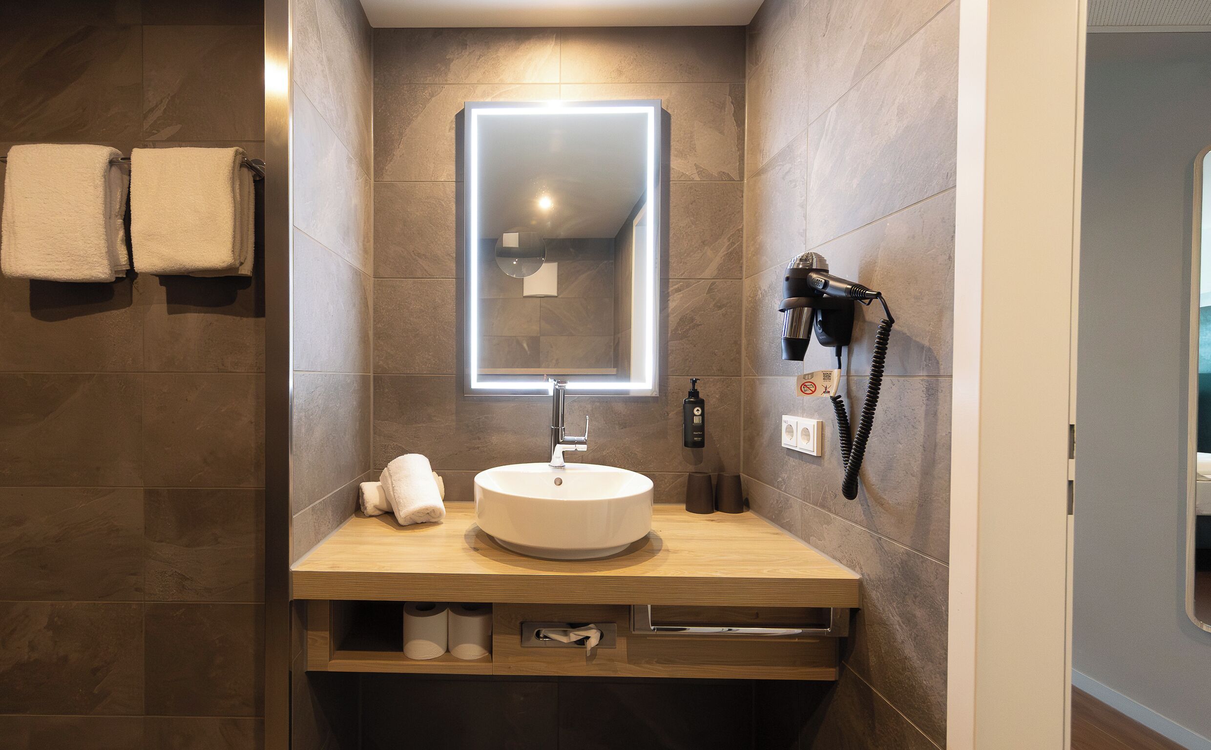 A modern bathroom with a round sink, a mirror, a hairdryer, and two towels on the wall.