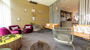 A modern hotel lobby with a wooden slat wall, seating areas, and a visible bar in the background. - DORMERO Hotel Freiburg (Freiburg im Breisgau)