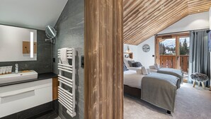 Une chambre moderne avec un grand lit, une salle de bain dotée d’un lavabo et d’un miroir blancs, et une vue sur l’extérieur.