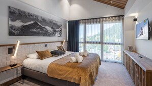 Une chambre moderne avec un grand lit, un tableau représentant une montagne, un téléviseur sur le thème du ski et une vue sur un paysage montagneux.