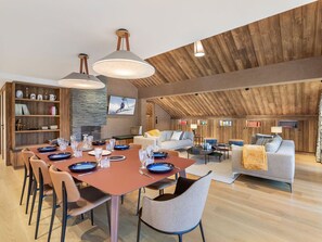 Uma sala de estar espaçosa com uma mesa de jantar posta para seis pessoas, um sofá e uma televisão na parede.
